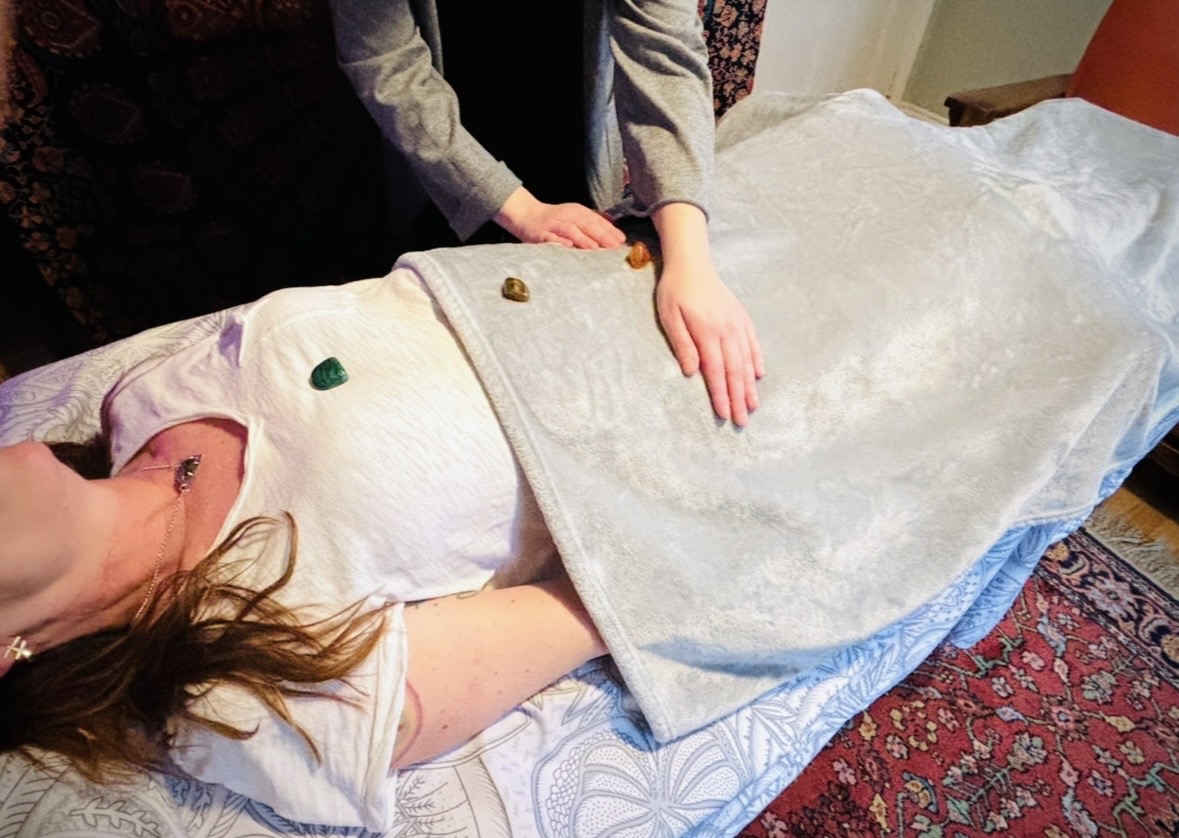 The Reiki practitioner's hands being placed on the client's sacral chakra, while the client is laying on a massage table