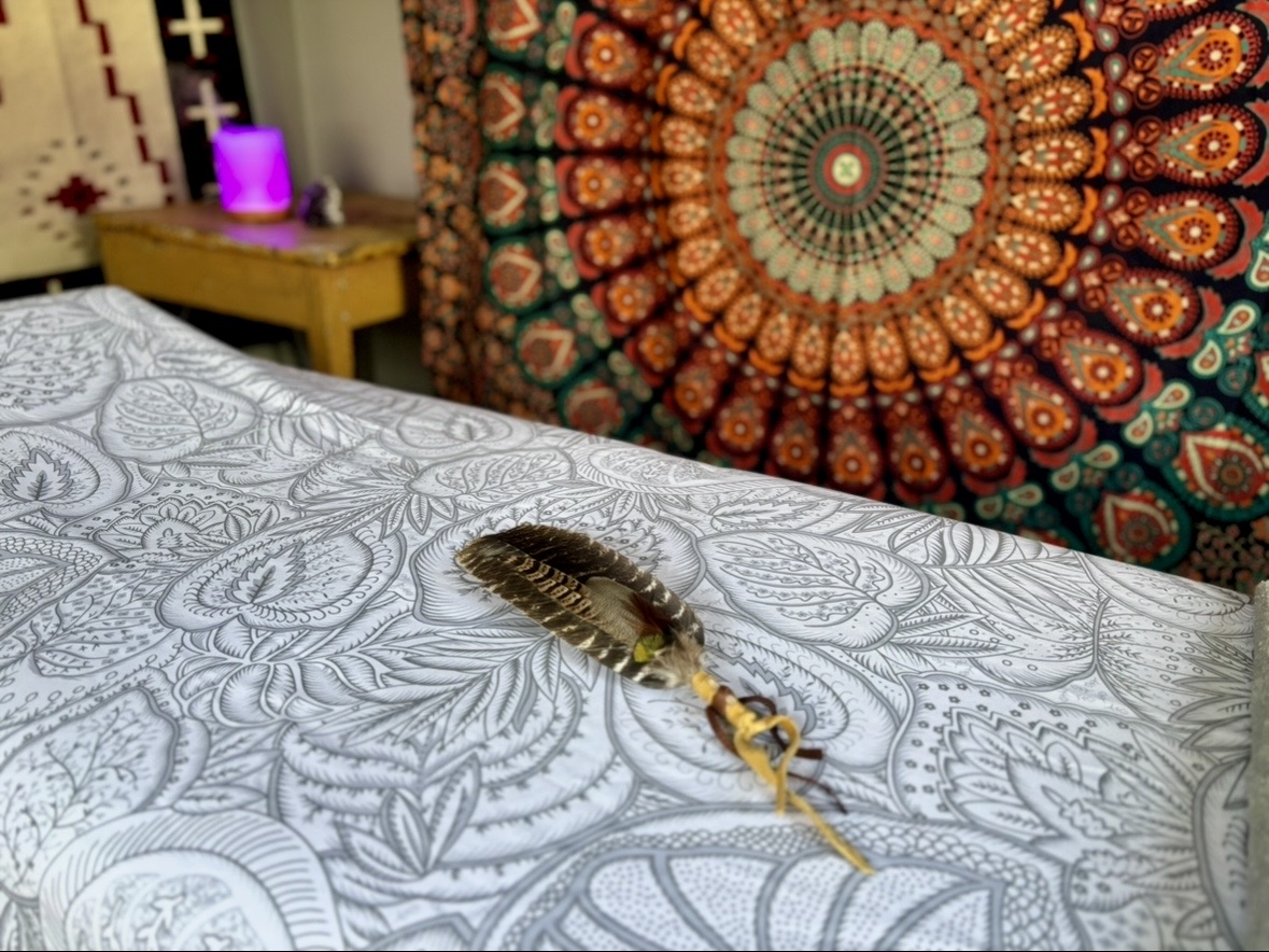 A feather laying still on a massage table with a decorative wall hanging in the background