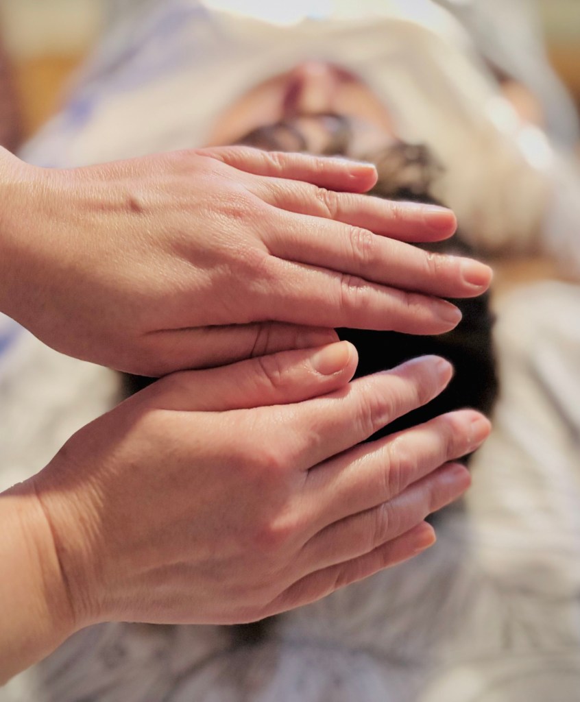 Hands being placed on a client's crown chakra